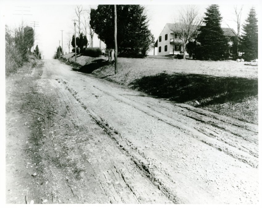 A black and white photo showing Brookville Road looking north, 1896, with a dirt road in the foreground and a farmhouse in the background.